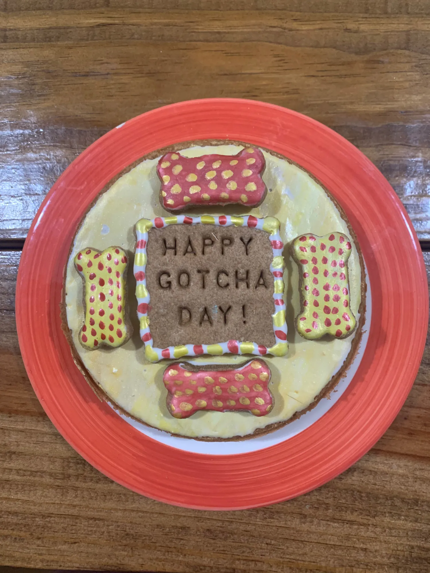 Gotcha day dog cake with yellow icing and pink polka dot bones on a coral plate